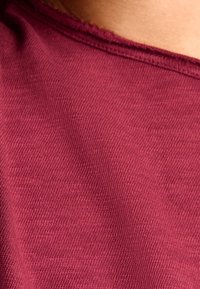 Bordowy materiał o delikatnej prążkowanej teksturze, charakteryzujący się gładkim, miękkim wykończeniem oraz okrągłym dekoltem z prostymi przeszyciami.