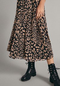 Zwart en beige luipaardprint jurk met een uitlopende zoom en knopen, gecombineerd met zwarte veterankle boots met gouden oogjes.