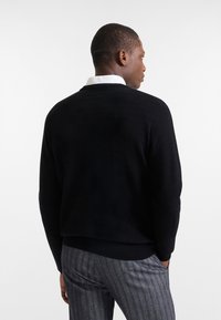 Maglione nero a trama con scollo rotondo, abbinato a pantaloni grigi a righe sottili. Il tessuto presenta un sottile motivo a zig zag e polsini a costine.
