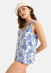 Blomsterstribet tanktop i hvid med blå blomster. Lavet af letvægtsstof. Har tynde stropper og en afslappet pasform.