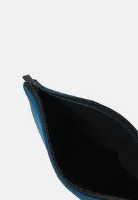 Pochette blu con zip aperta per mostrare l'interno nero vuoto, fotografata su uno sfondo chiaro e semplice.