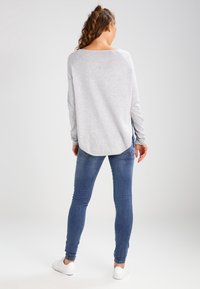 Szary długi rękaw top z zaokrąglonym dołem, połączony z niebieskimi rurkami i białymi sneakersami. Top ma luźny krój i miękką fakturę.