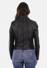 Giacca di pelle nera con design aderente, struttura slanciata e cuciture a contrasto. Abbinata a jeans di denim blu, con tasche in vista.