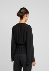 Černá halenka s dlouhým rukávem, se shromážděným pasem a kulatým výstřihem, vyrobená z hladké, lehké látky.