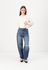 White, button-up, cropped sweater with embossed pattern; high-waisted, distressed blue jeans; black patent leather heels; minimalist beige handbag.