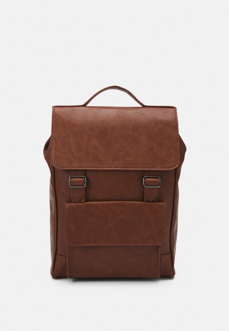 Zaino in pelle marrone con un cappuccio superiore, due fibbie, una tasca frontale e una maniglia. Texture liscia, forma rettangolare e design minimalista.