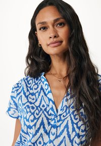 Camicia a maniche corte in tessuto blu e bianco con motivo, dotata di colletto button-down e texture leggera.