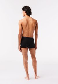 Boxer-briefs noirs avec une taille élastique, texture lisse et design ajusté, présentés sur un modèle de dos contre un fond uni.