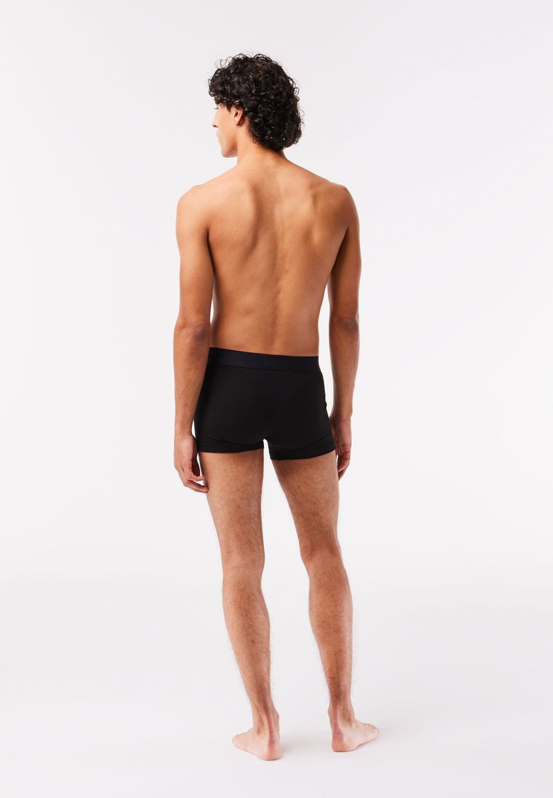 Schwarze Boxerbriefs mit elastischem Bund, glatter Textur und figurnahem Schnitt, hinter einem Modell von hinten vor einem einfarbigen Hintergrund präsentiert.