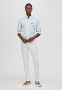 Camicia azzurra a righe con bottoni e taschino sul petto, abbinata a pantaloni bianchi e scarpe color beige. Tessuto morbido e vestibilità su misura.