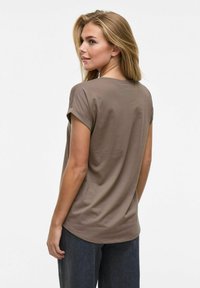 Camiseta marrón de manga corta hecha de una tela suave, con puños enrollados y un dobladillo redondeado. Combinada con pantalones de mezclilla oscuros.