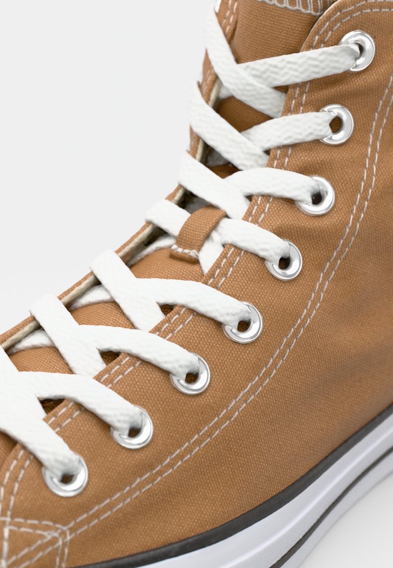 Zapatillas altas de lona en color marrón con ojales y cordones blancos. Cuentan con una suela plana y una franja negra como contraste en la parte inferior.
