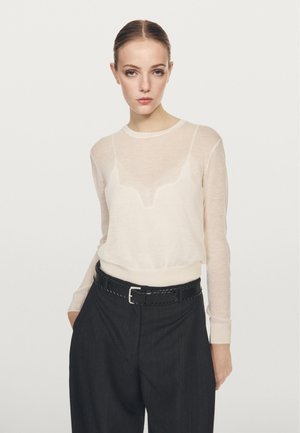 Light beige, semi-sheer long-sleeve top with a round neckline and ribbed cuffs, paired with high-waisted dark trousers and a woven black belt.