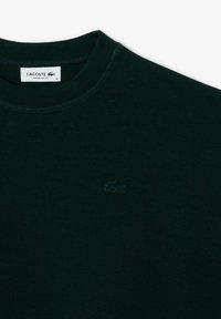 Tmavo zelené voľné tričko Lacoste s okrúhlym výstrihom a vyšitým krokodílím logom na hrudi.