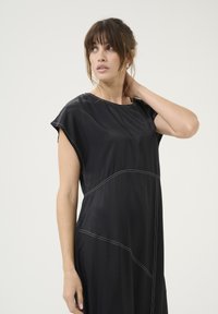 Must sulgeda must kleit, millel on lühikesed varrukad, sile tekstuur ja valged õmblused. Kujundus on asümmeetrilise lõike ja vabalt langevaga.