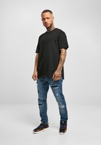 Svart bomullst-skjorte, kortermer, kombinert med blå slitte jeans. Skoene har mørke toner med oransje detaljer og en grov såle.