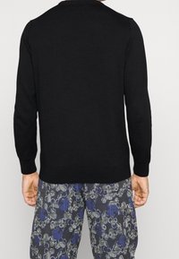 Pull noir à manches longues avec un col rond ; texture lisse ; associé à un pantalon bleu et gris à motifs floraux.