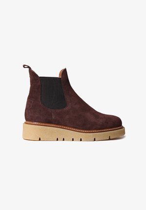 Bruine suede enkelboot met elastische zijkanten, ronde neus en een dikke, gestructureerde zool. Heeft contrasterende stiksels en een lusje om aan te trekken.