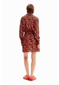 Kwiatowa sukienka z długimi rękawami, czarne tło, czerwone i pomarańczowe kwiaty, ściągnięta w talii, długość do kolan, połączona z wyrazistymi pomarańczowymi trampkami.