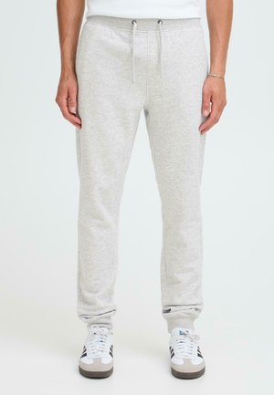 Gray sweatpants with elastic waistband and drawstrings, made of soft material. Features ribbed cuffs and side pockets. Paired with sneakers.