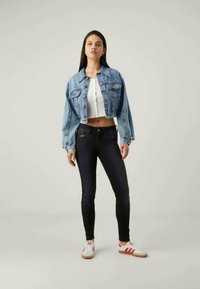 Denim jacket with light blue wash, cropped design; white fitted top, dark skinny jeans, and white sneakers with red accents.