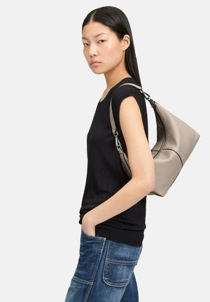 Haut côtelé noir associé à un jean bleu. Le mannequin porte un sac en cuir vegan gris clair et doux, de forme courbée et avec une sangle réglable.