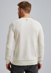 Crème gekleurde gebreide trui met lange mouwen, geribde manchetten en zoom. Heeft een klein logoaccent bij de achterkant van de hals.