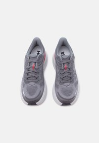 Ζευγάρι γκρι αθλητικά παπούτσια τρεξίματος με λευκές σόλες, πλέγμα υφάσματος, κορδόνια και κόκκινες λεπτομέρειες λογότυπου, σε θέα από πάνω σε λευκό φόντο.