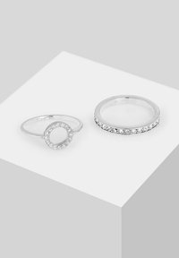 Sølvstabelringe med en flad ring med klare sten og en cirkulær accent med sten. Glat, poleret overflade med en skinnende finish.