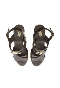Brown leather sandals with crossed straps, an ankle buckle, and a round gold accent. Smooth texture with a flat sole.