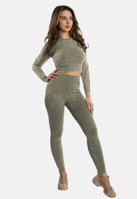 Top lungo a maniche lunghe verde corto abbinato a leggings a vita alta dello stesso colore. Entrambi presentano un tessuto texturizzato e leggermente marmorizzato.