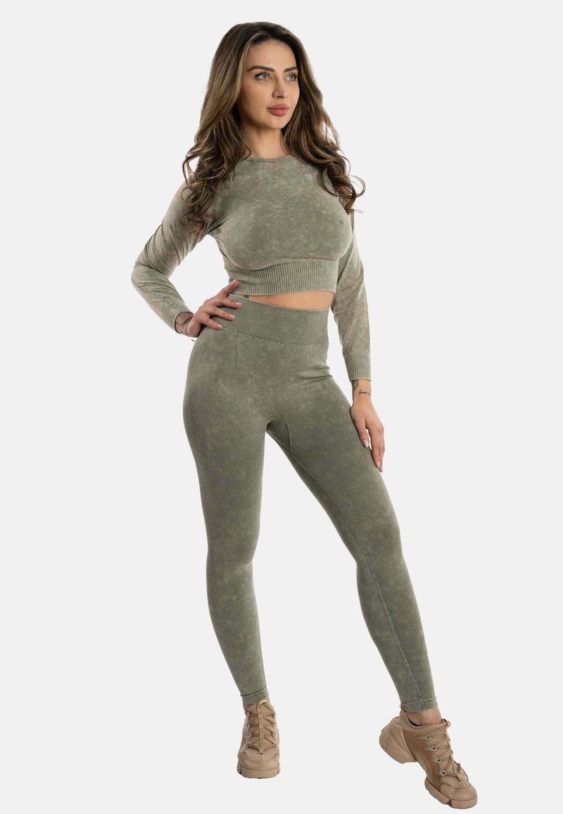 Top lungo a maniche lunghe verde corto abbinato a leggings a vita alta dello stesso colore. Entrambi presentano un tessuto texturizzato e leggermente marmorizzato.