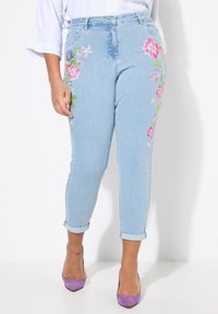 Světle modré džíny s květinovou výšivkou na stranách, se zúženým střihem nohavic, ohrnutými lemy a středním pasem.