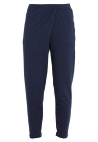 Pantalons de jogging bleu marine en tissu doux, avec un design de taille croisée et un petit logo noir sur le côté gauche.