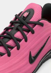 Roosa spordikeel, millel on tekstuuriga võrgusilm üleosa, mustad paelad ja läikiv must swoosh logo küljel. Detailne disain kontsapooles.