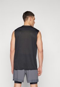 Sort ærmeløs træningstop lavet af åndbart mesh materiale, parret med grå shorts med kontrasttekstur og trim detaljer.