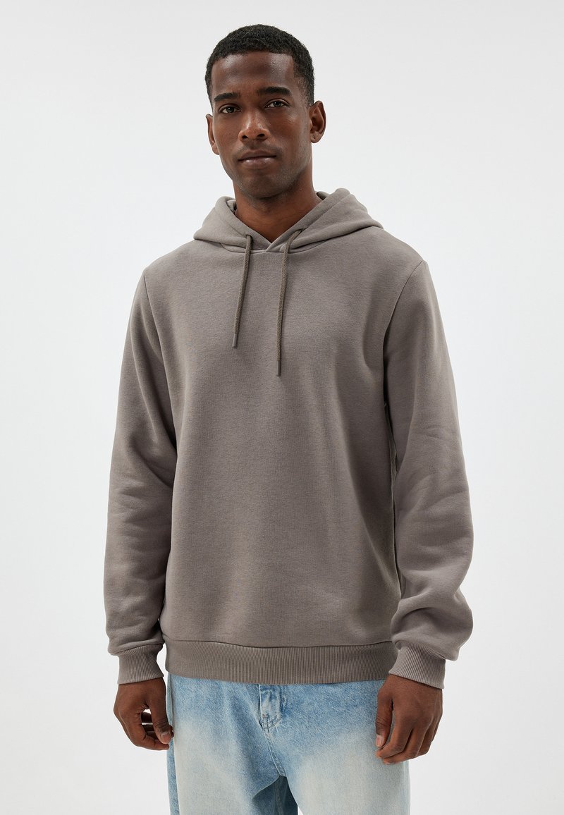 Grauer Hoodie mit Kordeln, gerippten Bündchen und Bund. Weiche Textur, lockerer Schnitt, kombiniert mit verwaschenen blauen Jeans.