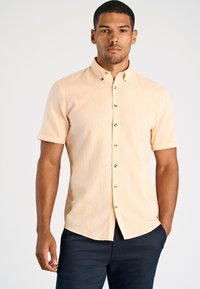 Korte mouw, knoopsluiting overhemd in licht perzikkleurige stof met een subtiele textuur en contrasterende knopen, gecombineerd met donkerblauwe broek.