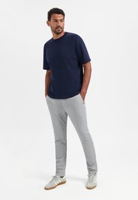 Marineblauw T-shirt met korte mouwen, gecombineerd met lichte grijze tapered broek, gedragen met grijze sneakers met witte en zwarte accenten.