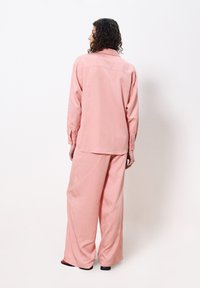 Pink oversized shirt and wide-leg pants in a soft fabric, featuring a buttoned collar and relaxed silhouette. Simple, solid color design.