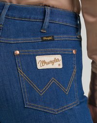 Jeans in denim blu slim fit con una toppa in pelle color tan, cuciture dorate e distintivo ricamo a 'W' sulla tasca posteriore.