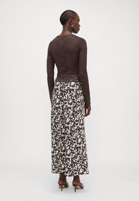 Long-sleeve brown lace top paired with a flowy white and brown patterned maxi skirt. Model wears brown high-heeled shoes.