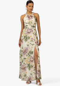 Robe maxi en tissu léger, ornée d'un motif floral avec des fleurs violettes et jaunes, décolleté halter et fente sur le côté ; sandales de couleur neutre.