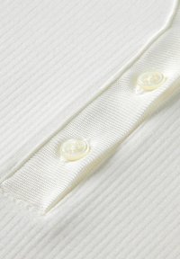 Close-up van witte ribbelstof met een gladde knoopsluiting die twee doorzichtige witte knopen heeft genaaid.