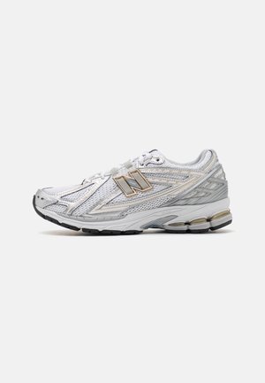 Chaussure de sport blanche et grise avec des panneaux en mesh, semelle amortissante, fermeture à lacets et logo New Balance sur le côté, montrée de profil.