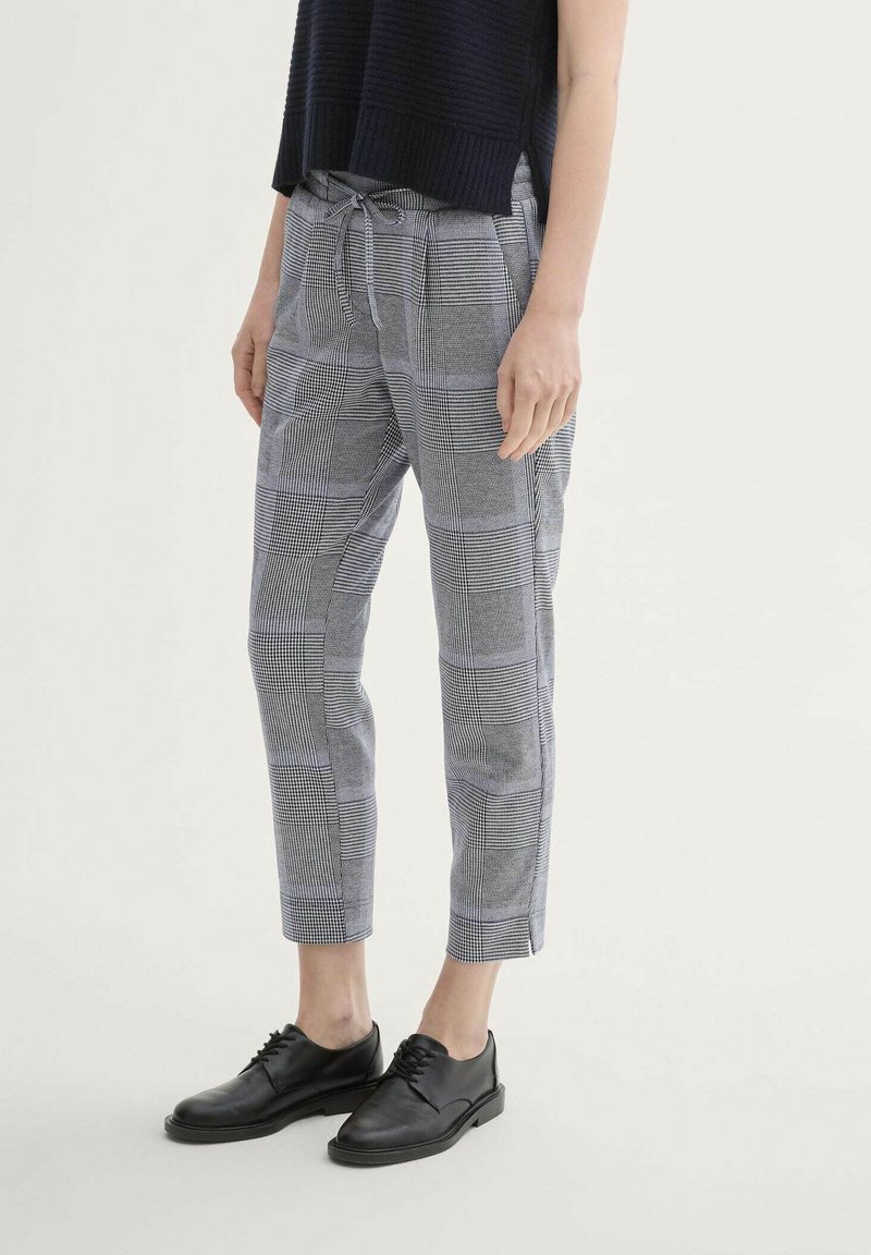 Grijze geblokte broek met een trekkoord in de taille, met een relaxed fit en een verkorte lengte. Gecombineerd met zwarte leren schoenen.