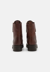Botas de piel marrón hasta el tobillo con textura suave, punta redonda y tacón bajo tipo bloque. Presentan un asa en la parte trasera y un detalle de costura minimalista.