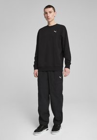 Czarna bluza z okrągłym dekoltem, z białym logo na piersi, połączona z czarnymi spodniami cargo i czarnymi trampkami z białą podeszwą.