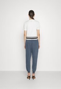 White short-sleeve top with a black striped hem paired with blue jogger pants. Displaying a smooth texture and casual fit.