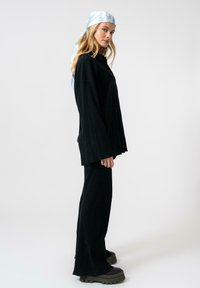 Top nero a coste con maniche ampie e pantaloni a palazzo abbinati, abbinati a un foulard in satin azzurro chiaro con un motivo testuale.